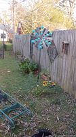 Photo showing two large metal windmills with blue accents standing in an outdoor yard next to a wooden fence and garden plants.