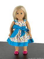 Front view of the 18-inch American Girl doll with blonde hair, blue eyes, floral homemade dress with blue bow, and pink shoes.