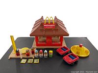 Full set displayed showing McDonald's building, 7 wooden figures, 3 meal plates, 2 cars, yellow play ride, and McDonald's sign detached from stand.