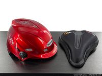 Photo of red bicycle helmet and black foam padded seat cover side by side on black surface.