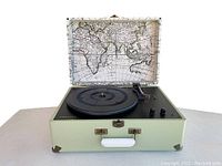 Front open view of Crosley Keepsake USB turntable with old world style map design visible on the inside lid, light green suitcase casing, and black turntable platter with tone arm and control knobs.