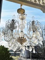 Front and side view of the six-arm lucite acrylic prism chandelier in a daytime outdoor setting, showing the clear hanging prisms and decorative arms.