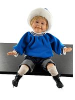 Front view of porcelain doll seated, showing full outfit including blue top, denim pants, white socks, and black ice skates