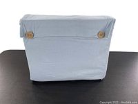 Light blue cotton sheet set neatly folded and buttoned on a flat surface, showing front side with two wooden buttons on each side.