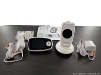 Photo showing the video monitor, projection camera on round base, two power adapters with cords, and instruction manual.