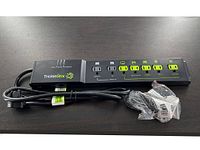 Full view of TrickleStar 7 outlet power strip showing the unit and power cord with plug, placed on a dark surface.