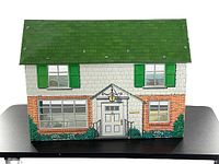 Front view of the vintage tin metal dollhouse showing green roof, brick and shuttered facade.