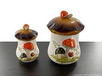 Photo shows both mushroom-shaped canisters side by side from front view, detailing colorful mushroom decorations.