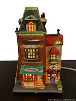 Front view of Dorothy's Dress Shop collectible showing brick facade, green awning, and lit windows with Christmas decoration
