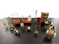 Overview of entire vintage miniature brass dollhouse furniture set including beds, chairs, mirror, clock, sewing machine, and plush accessories arranged on a table.