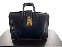 Front view of the black leather doctor's satchel with brass combination lock and reinforced corners.