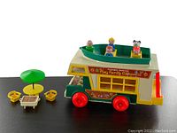 Side view of Fisher Price camper with detachable boat holding the Fisher Price figures and dog figure, patio accessories set beside it.