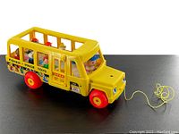 Photo showing the vintage Fisher Price yellow school bus with red wheels, decals, pull string at front, and seven Little People figures seated inside visible through open sides.