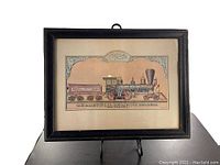 Framed vintage graphic train illustration shown full front with a black wooden frame and easel stand.
