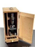 Microscope inside original wooden case with door open and drawer pulled out showing storage space.