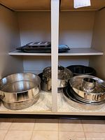 Photo of shelving with multiple bakeware items including bundt pans, springform pan, muffin tin, cooling rack, and cake pans