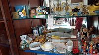Display of multiple bee-themed items including a book, glass jars, bear figurines, ashtrays, and other collectibles on glass shelving inside a cabinet