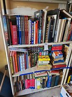 Two shelves filled with multiple rows of books arranged vertically and stacked horizontally; includes large hardcover books and smaller paperbacks in varying colors and designs