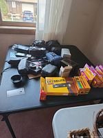 Overview of all vintage cameras, film packs, vintage cell phone, binoculars, and accessories laid out on black table.
