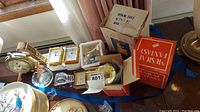 Table display of clocks, boxed music boxes, and ashtray with overall lot items visible.