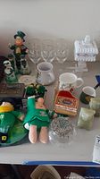 Full assortment of lot items including figurines, glassware, mugs, music box, and boxes shown together on table surface.