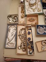Overview of assorted costume jewelry pieces including bracelets, necklaces, brooches, and earrings displayed in boxes.