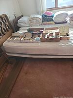 Overview of multiple trays and boxes of assorted jewelry items including necklaces, rings, earrings, and bracelets placed on top of a bed.
