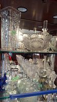 Shelf with various cut and pressed glass items including vase, bowls, glasses, salt and pepper shakers, and decanter.