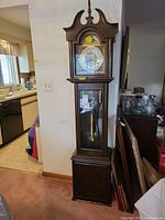 Full front view of the Daneker grandfather clock showing the wooden case, glass panel, and clock face.