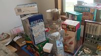 Various boxed and unpacked kitchen appliances and accessories including Brita water pitcher, food processor, mixers, knife block, and scale displayed on table