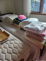 Display of assorted afghans, blankets, and comforters stacked on a bed next to a partially visible mattress.