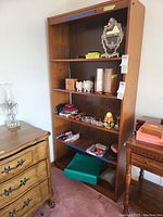 Wooden shelving unit with various items including a vintage oval mirror on top shelf, stack of boxes, piggy bank, cut glass items, brushes, and boxed mirrors on different shelves.