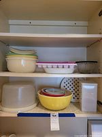 Photo showing shelves with various Pyrex mixing bowls, nested smaller bowls, pie plates, ice cube tray, and other kitchen storage containers