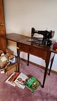 Full view of vintage Singer sewing machine on extended wooden cabinet with sewing books and accessories on floor.