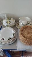 Overview of floral designed soup set including ceramic tureen, bowls, plates, and wicker baskets on table