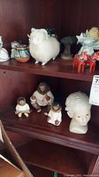 Top shelf with white fluffy sheep figure, colorful ceramic pot, small animal figurines, and painted wooden horses