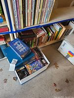 Shelf with a variety of books including the Reader's Digest Home Front book, and a box of VHS tapes on the floor featuring children's story titles like Peter Pan
