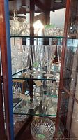 Photo showing multiple items inside a glass cabinet including tall cut glass pilsner glasses and other glassware pieces.