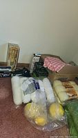 Photo showing several skeins and balls of yarn in white, yellow colors, and a box filled with fabric including a pink checkered cloth on top along with some boxed steamers and irons.