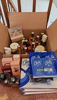 Open cardboard box showing multiple glass fragrance bottles, boxed cologne packs, gift sets, skincare boxes