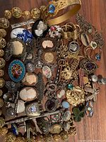 Overall assortment of jewelry on wooden surface showing brooches, pendants, necklaces, bracelets and lockets