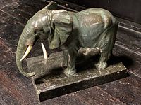 Side view of antique solid bronze elephant sculpture on rectangular onyx base showing ivory tusks and detailed textured skin.