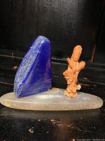 Three-piece set (coral figurine, lapis lazuli, agate base) on black background, angled view