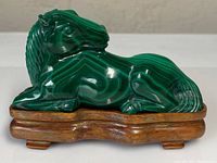 Front view of the carved malachite horse on a wooden stand showing smooth polished surface and green banded stone details.