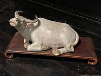 Full view of porcelain bull on hardwood stand showing the entire figurine and base.