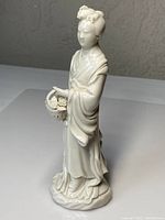 Front right-side view of the porcelain figure showing detailed basket and robe folds