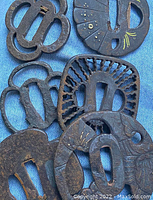 Top view of eight iron tsuba laid on denim showing varied shapes and openwork