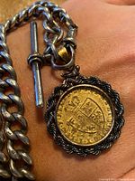 Full view of curb link chain, T-bar and coin fob pendant laid on wrist