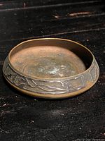 Side angle showing the copper dish with silver overlay band featuring floral motif.