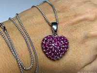 Front view of hand displaying heart-shaped pendant with dense cluster of genuine rubies on sterling silver chain.